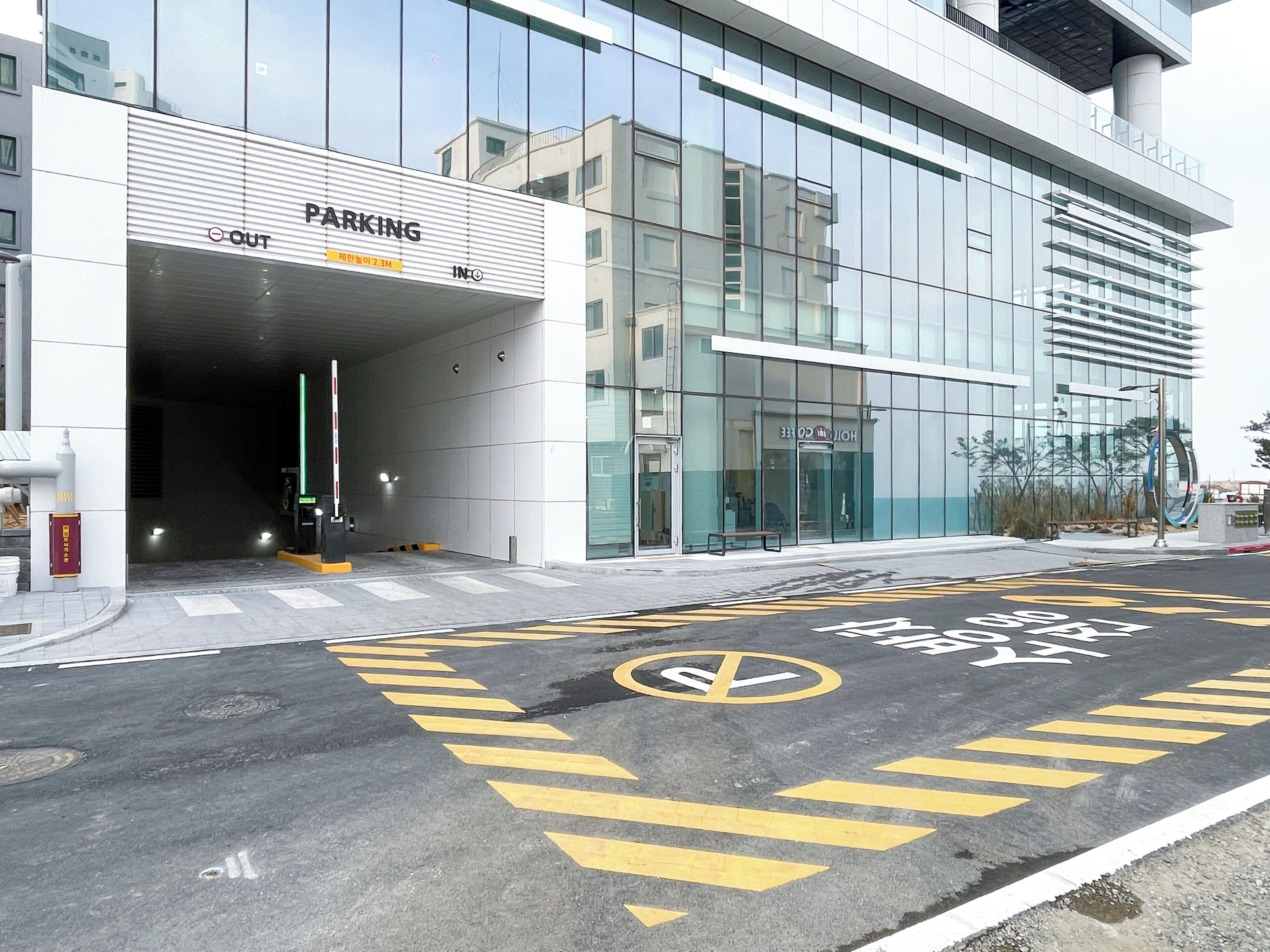 Un edificio moderno con fachada de vidrio, entrada para estacionamiento y un paso de peatones bien señalizado.