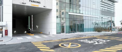 Un edificio moderno con fachada de vidrio, entrada para estacionamiento y un paso de peatones bien señalizado.
