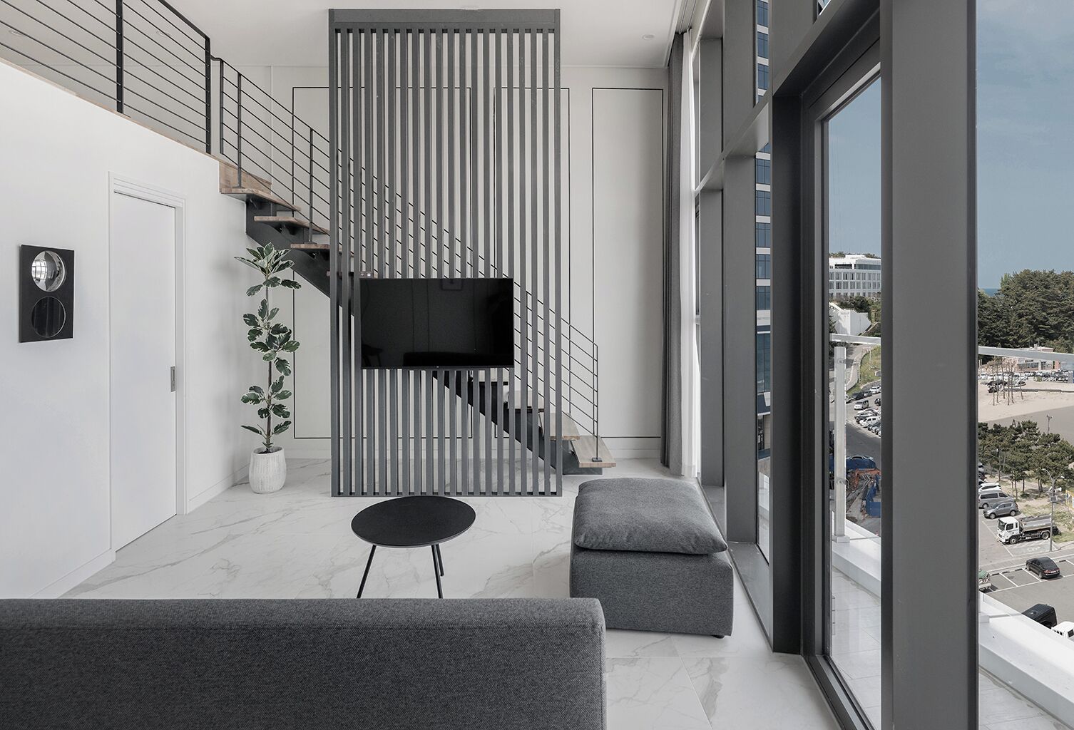 Ein modernes Wohnzimmer mit Fernseher, Treppe, einer Sitzecke und Blick auf die Stadt.