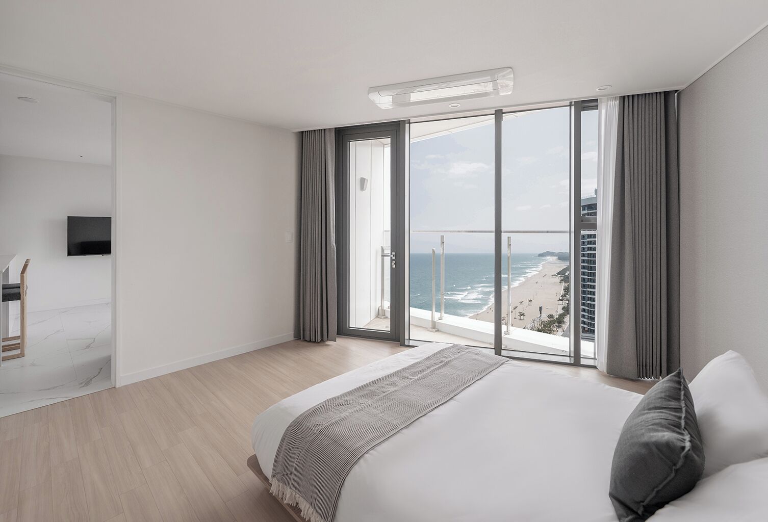 A modern hotel room with a large bed, a TV, a balcony with a city view, and a sliding door.