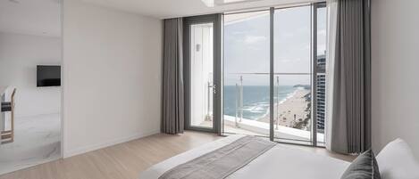 A modern hotel room with a large bed, a TV, a balcony with a city view, and a sliding door.