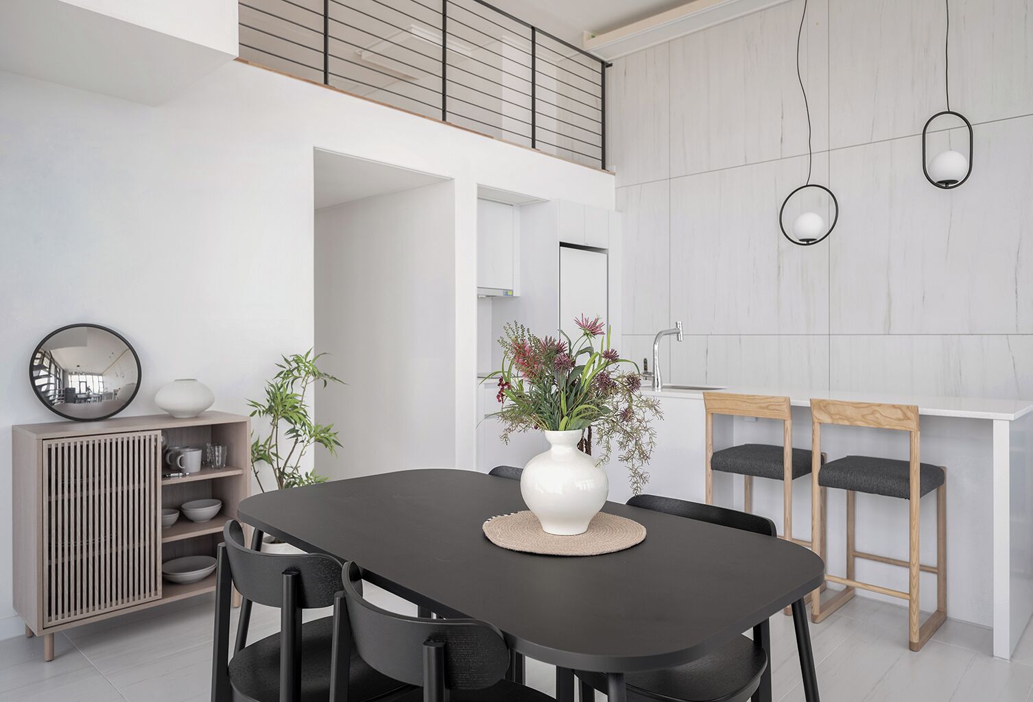 Un comedor moderno con una mesa oscura, sillas negras, un jarrón blanco con flores y un aparador de madera con estantes.