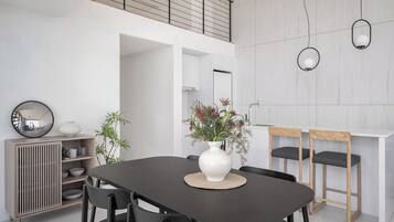 Un comedor moderno con una mesa oscura, sillas negras, un jarrón blanco con flores y un aparador de madera con estantes.