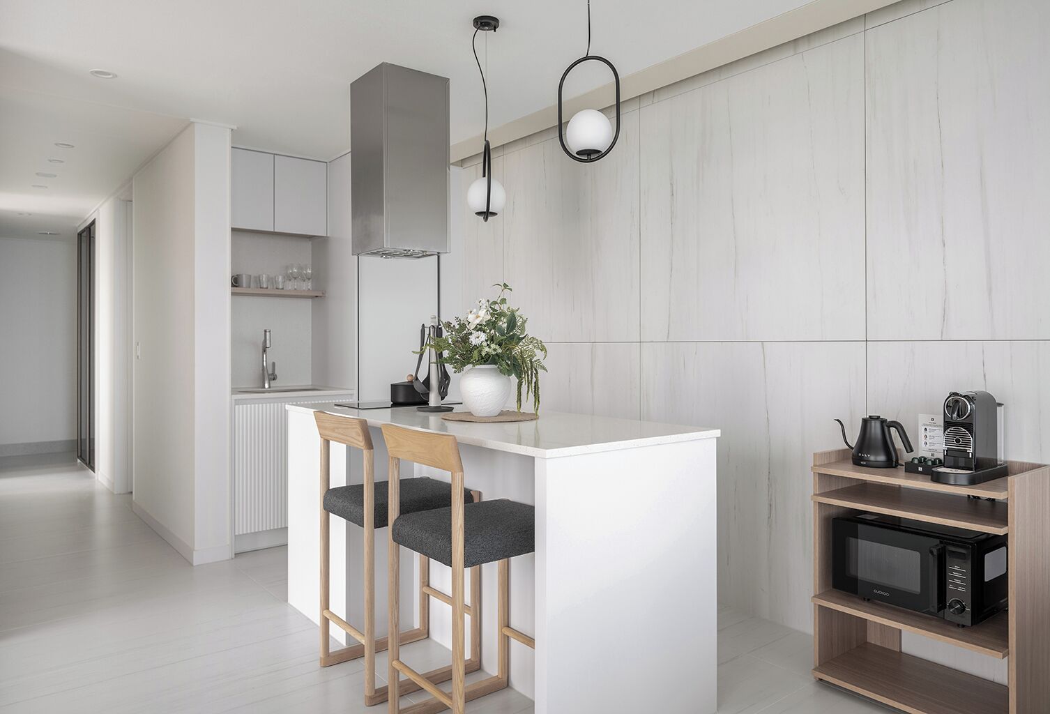Eine moderne Küche mit einer weißen Kücheninsel, Holzstühlen, einer Kaffeemaschine und einer Mikrowelle auf einem Holzboden.