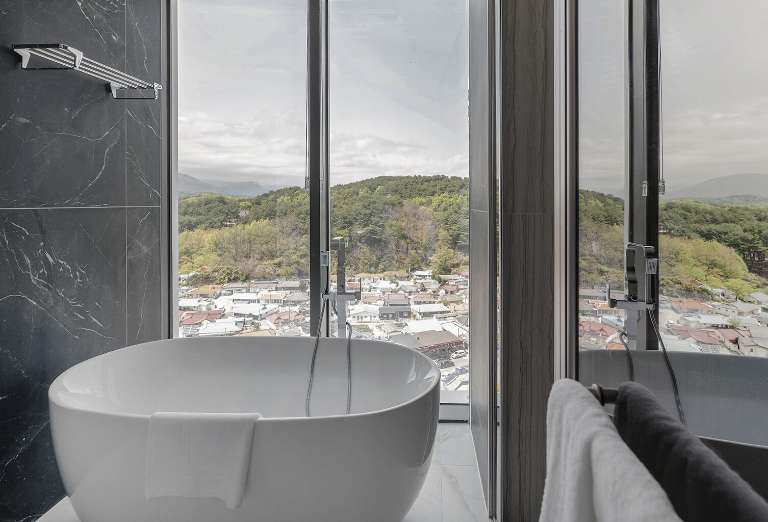 A modern bathroom with a large freestanding bathtub, a glass shower enclosure, and a view of a cityscape through large windows.