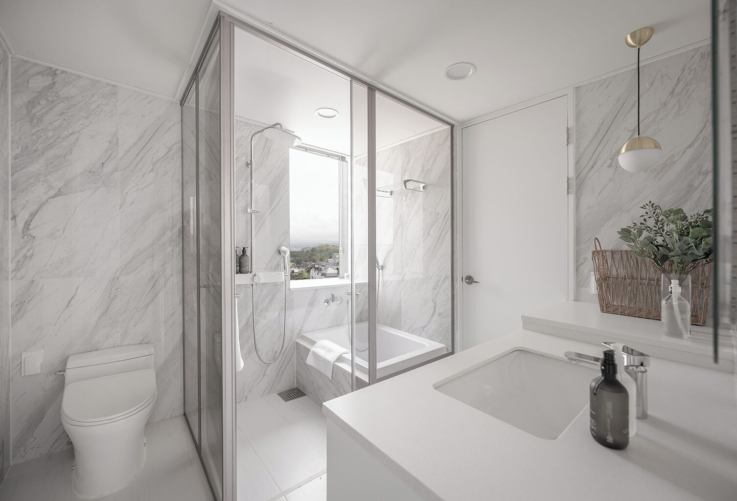 Een moderne badkamer met een douchecabine van glas, een wit toilet, een groot wastafel en een spiegel met een plant.