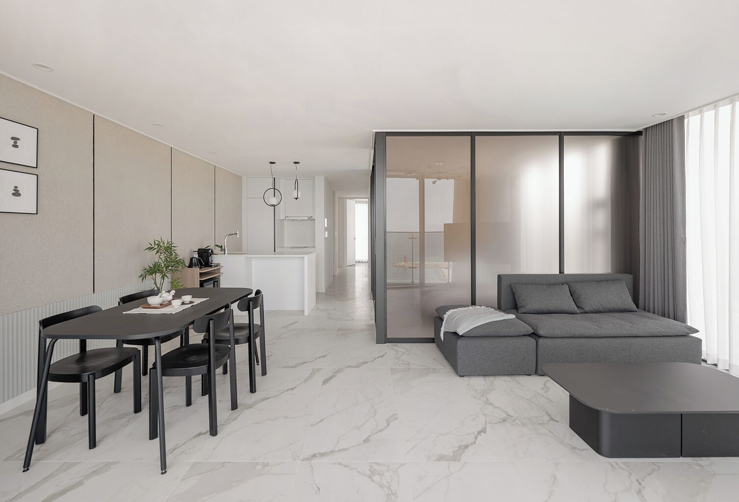 A modern living room with a grey sofa, a dining area with a table and chairs, and a kitchen in the background.