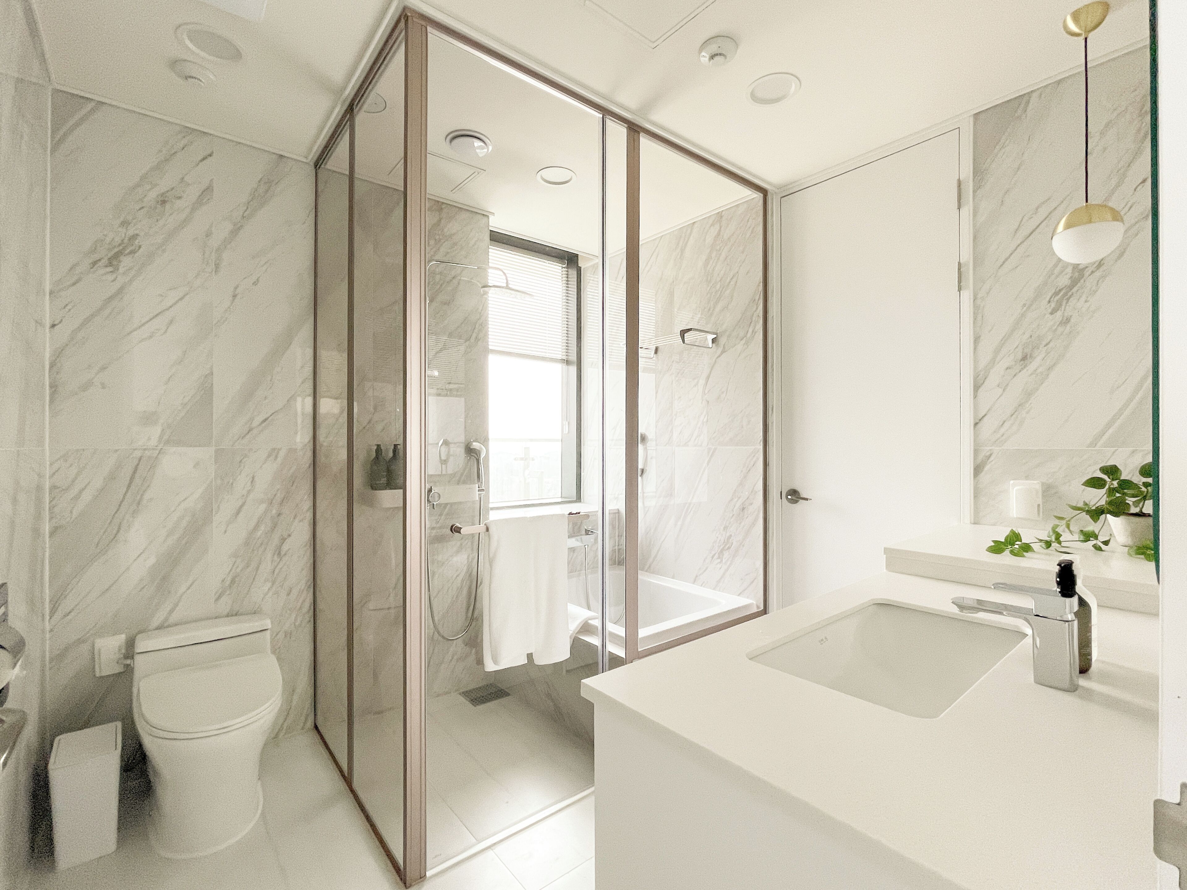 A modern bathroom with a glass-enclosed shower, a white sink, and a marble-tiled wall.