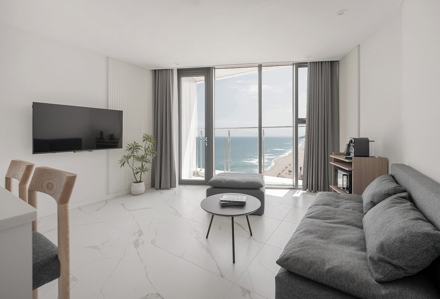 A modern living room with a TV, seating, a plant, and a view of the ocean.