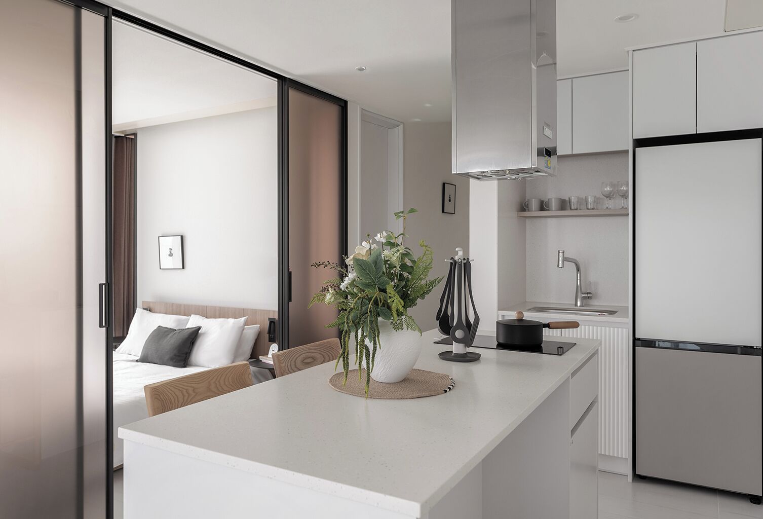 A modern kitchen with a central island, a dining area with a sofa, and a bedroom with a bed and a window.