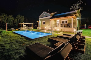 Ein Haus mit Swimmingpool, Liegestühlen im Freien und einer überdachten Sitzgelegenheit.