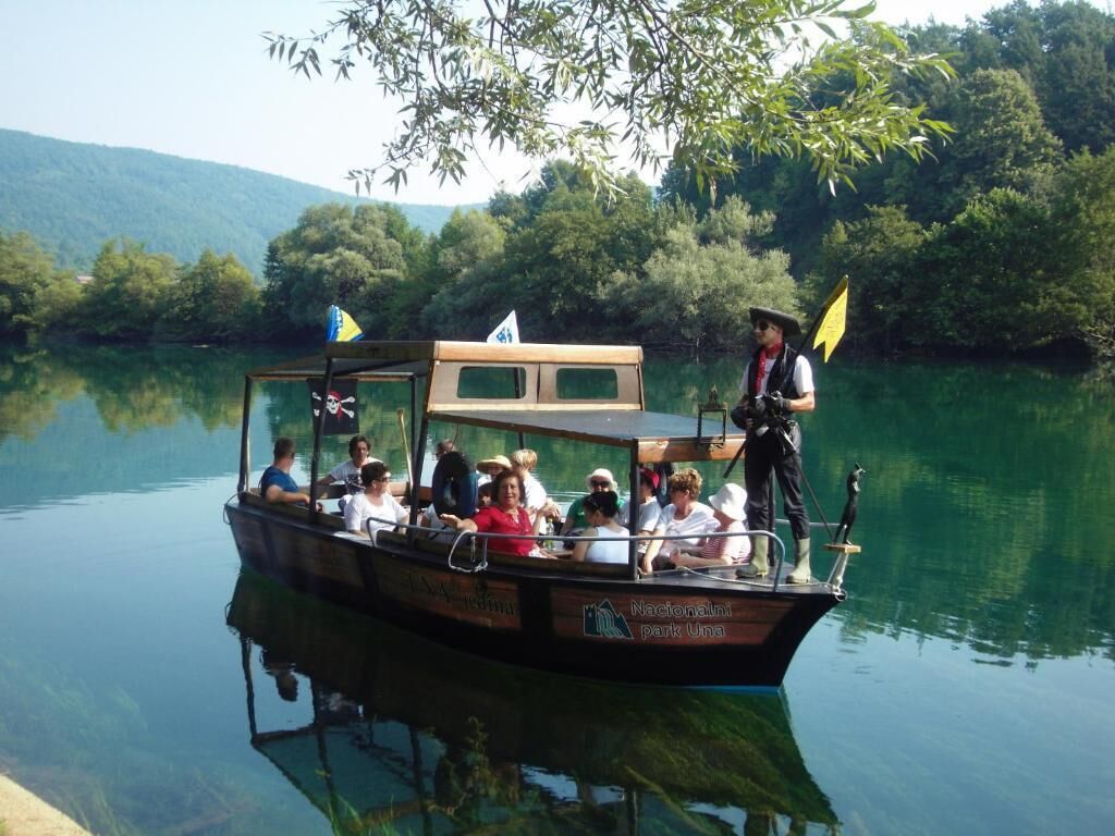 A boat with passengers and a guide, docked at a calm lake with greenery in the background.
