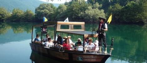 A boat with passengers and a guide, docked at a calm lake with greenery in the background.