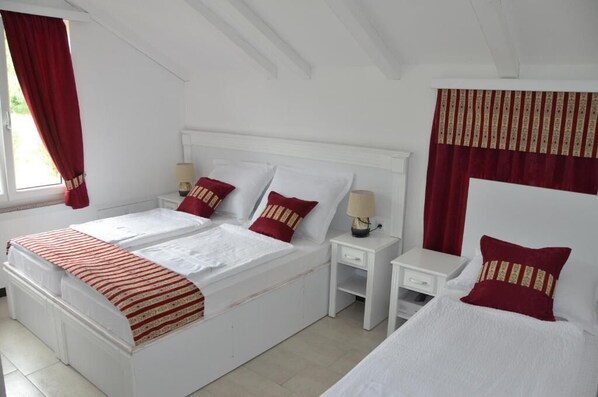 A double bed with two pillows, a bedside table with a lamp, and a window with red curtains. - Hotel Neron i River View (Bihać)