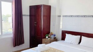 Ένα δωμάτιο ξενοδοχείου με ένα μεγάλο κρεβάτι, μια ντουλάπα, ένα κομοδίνο με είδη προσωπικής υγιεινής και ένα παράθυρο με κουρτίνες.