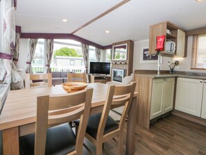A compact kitchen with a dining area, a TV, and a fireplace. - 49 Cader Idris, Hafan-y-mor Holiday Park (Pwllheli)