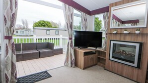 A covered outdoor area with a sofa, a flat-screen TV, and a fireplace. - 49 Cader Idris, Hafan-y-mor Holiday Park (Pwllheli)