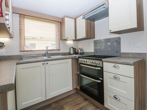 A compact kitchen with a sink, stove, oven, and a toaster. - 49 Cader Idris, Hafan-y-mor Holiday Park (Pwllheli)