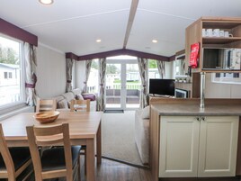 A room with a dining table, chairs, a sofa, a television, and a kitchen area with cabinets and a microwave.