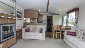 A cozy living area with a sofa, a fireplace, a dining table, and a kitchen in the background. - 49 Cader Idris, Hafan-y-mor Holiday Park (Pwllheli)