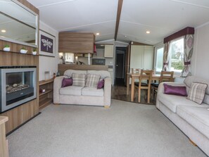 A cozy living area with a sofa, a fireplace, a dining table, and a kitchen in the background. - 49 Cader Idris, Hafan-y-mor Holiday Park (Pwllheli)