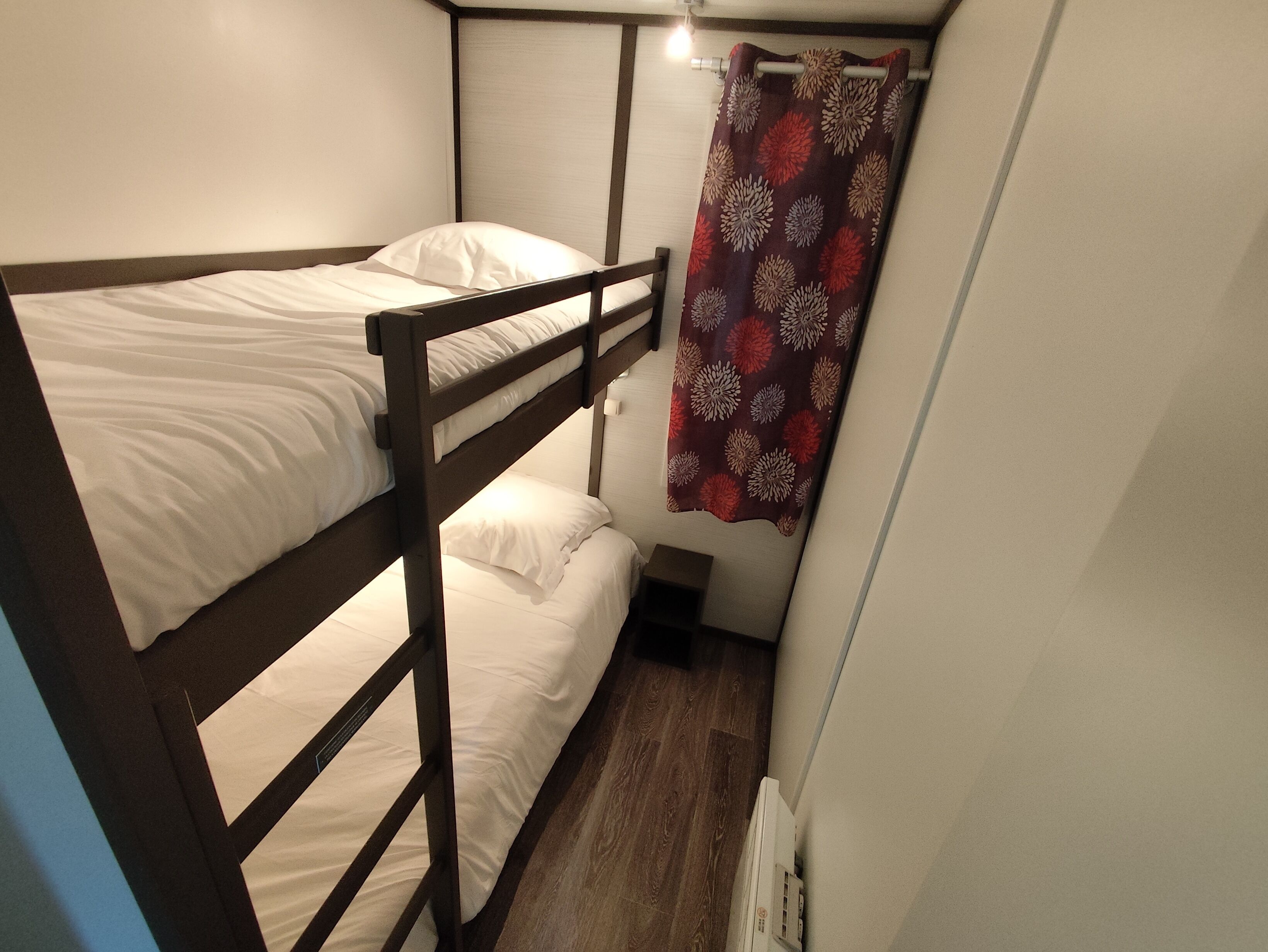 A bunk bed room with a wooden frame, white bedding, and a floral curtain.