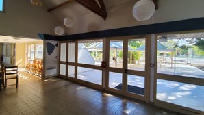 A spacious indoor area with a tiled floor, large windows, and a view of an outdoor patio area.