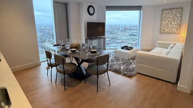 Um espaço moderno com área de refeições, sofá, TV e vista para a cidade.