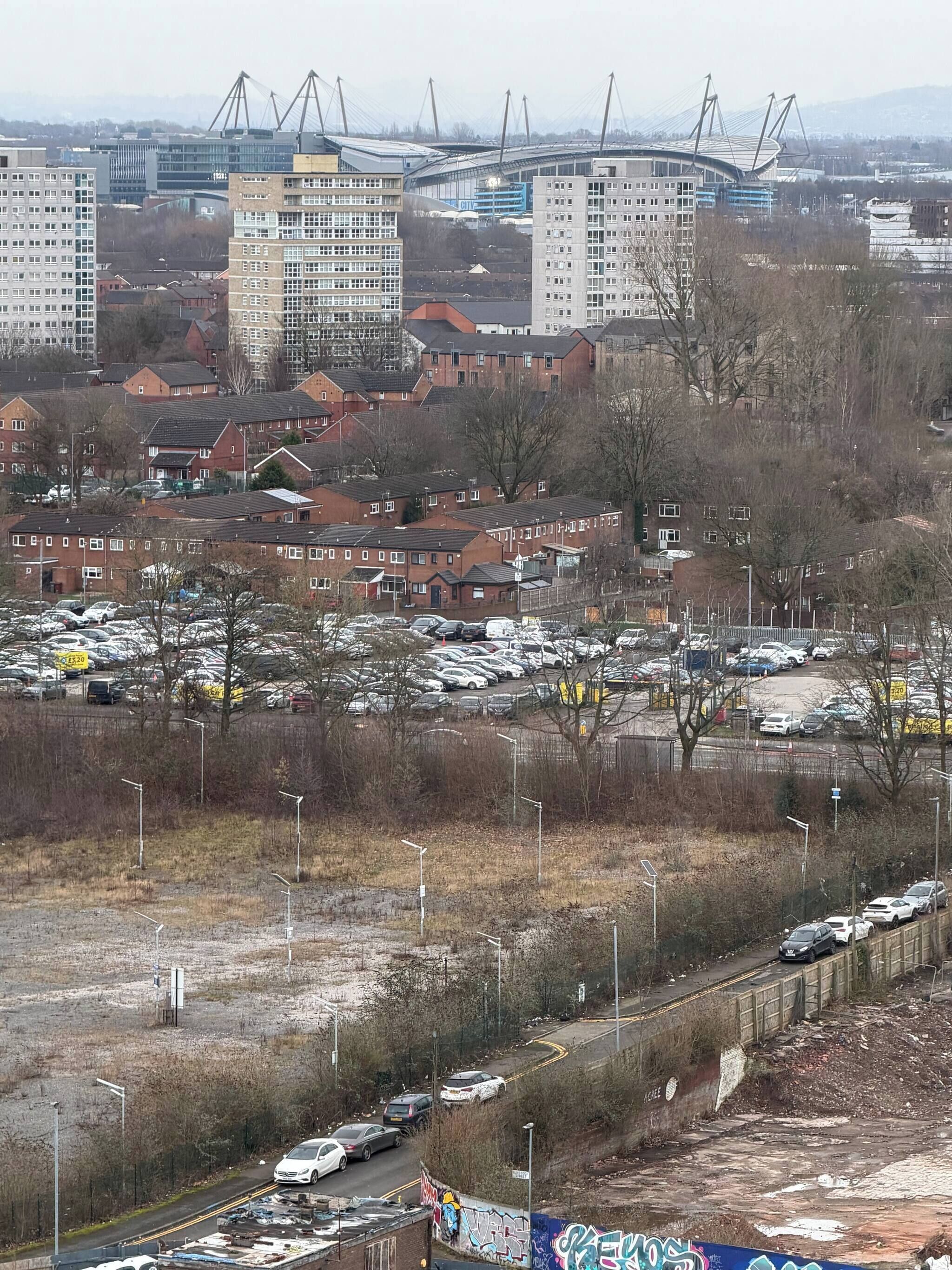 A residential area with multiple apartment buildings, a parking lot with cars, and a bridge in the background.