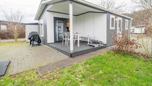 Ein modernes, eingeschossiges Gebäude mit einer überdachten Terrasse, einer kleinen Sitzecke im Freien und einer sichtbaren Tür.