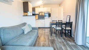 Ein kompakter Wohnbereich mit Sofa, Esstisch, Stühlen, Küchenzeile und einem fensterbepflanzten Fenster.