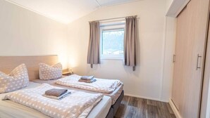 Ein Schlafzimmer mit zwei Betten, einem fensterbelaubten Fenster, einem Kleiderschrank und einem Nachttisch mit Lampe.
