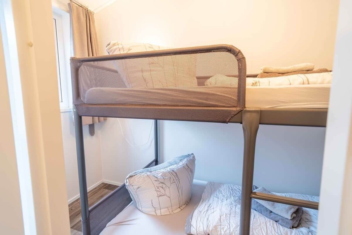 Un lit superposé avec une tête de lit en treillis, un oreiller et une couverture sur le lit du bas.