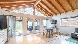 Eine geräumige Küche mit großem Fenster, ein Essbereich mit Tisch und Stühlen sowie ein graues Sofa.