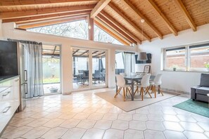 Eine geräumige Küche mit großem Fenster, ein Essbereich mit Tisch und Stühlen sowie ein graues Sofa.