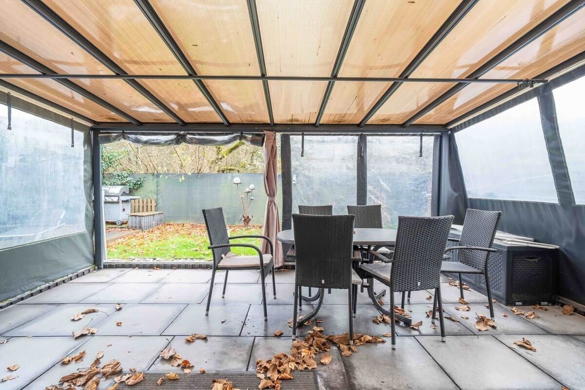 Ein überdachter Patio-Bereich mit Tisch und Stühlen und Blick auf einen Garten.