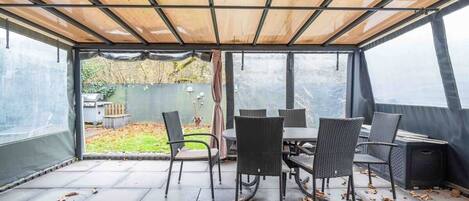Ein überdachter Patio-Bereich mit Tisch und Stühlen und Blick auf einen Garten.