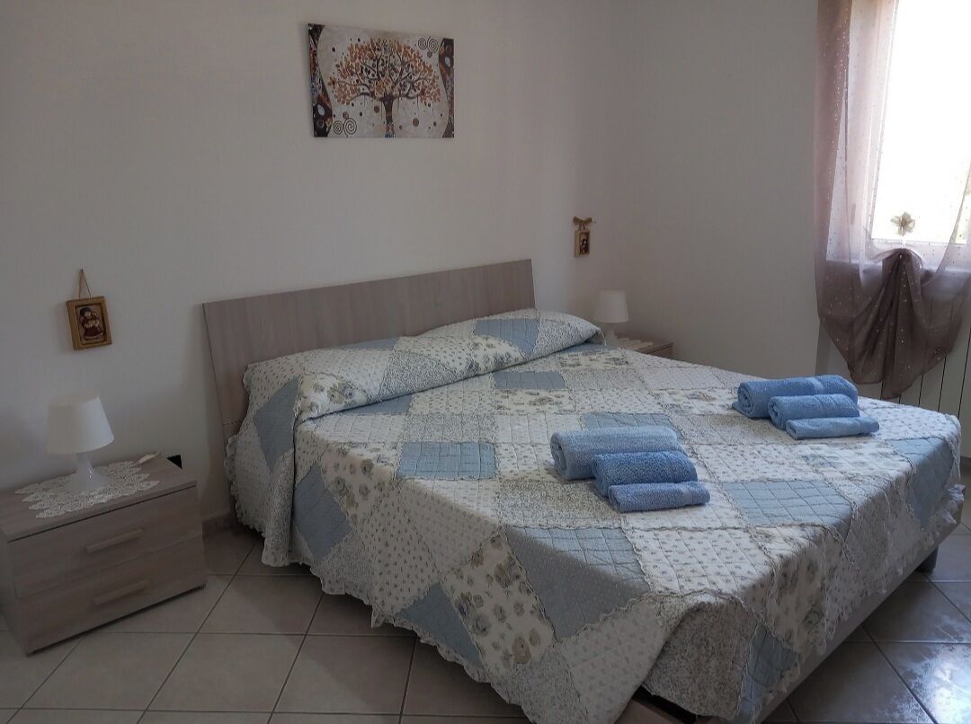 A bedroom with a bed, nightstand, lamp, and a painting on the wall.