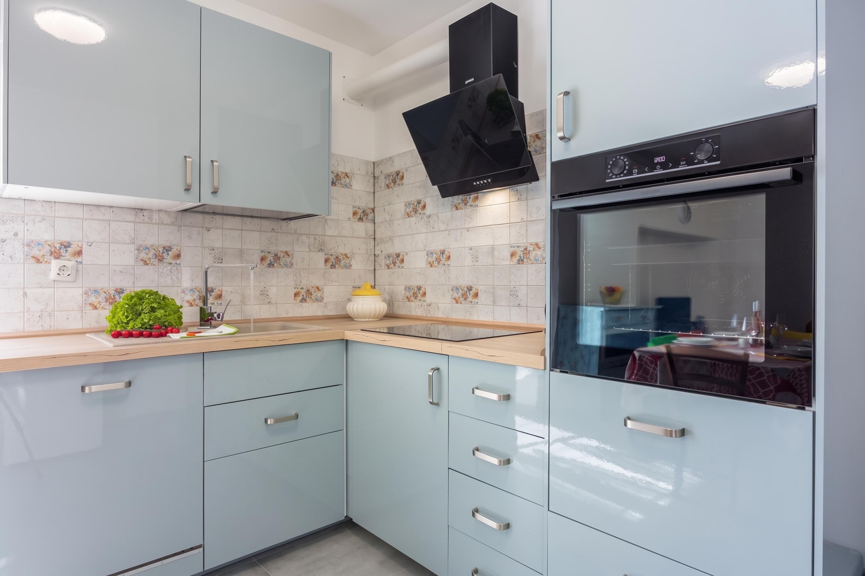 A modern kitchen with light blue cabinets, a black range hood, and a tiled backsplash.