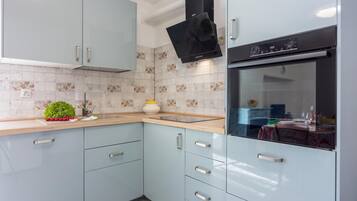 A modern kitchen with light blue cabinets, a black range hood, and a tiled backsplash.