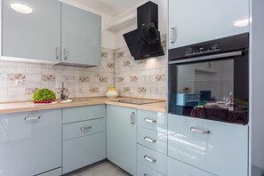 A modern kitchen with light blue cabinets, a black range hood, and a tiled backsplash. - Rural Apt Arya: Garden & BBQ (Koper)