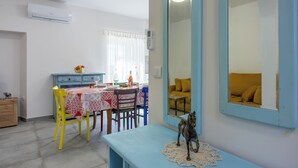 Un comedor con una mesa dispuesta para dos, un banco azul, un espejo grande y una ventana con cortinas.