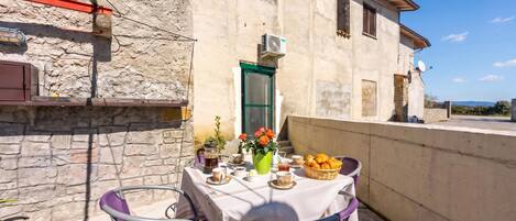 A balcony with a table set for breakfast, including croissants, a coffee pot, and a vase with flowers.