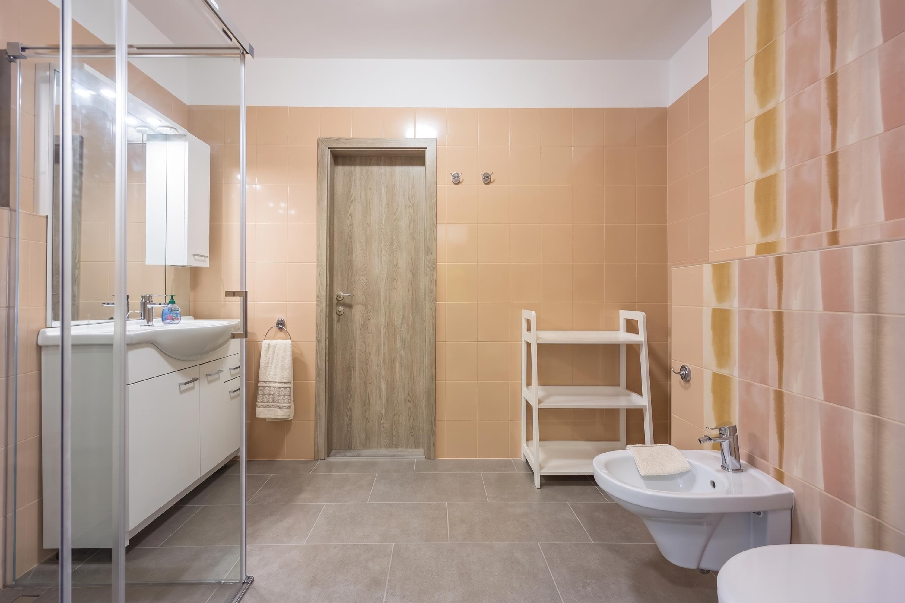 Een moderne badkamer met een douchecabine van glas, een witte wastafel, een toilet en een houten deur.