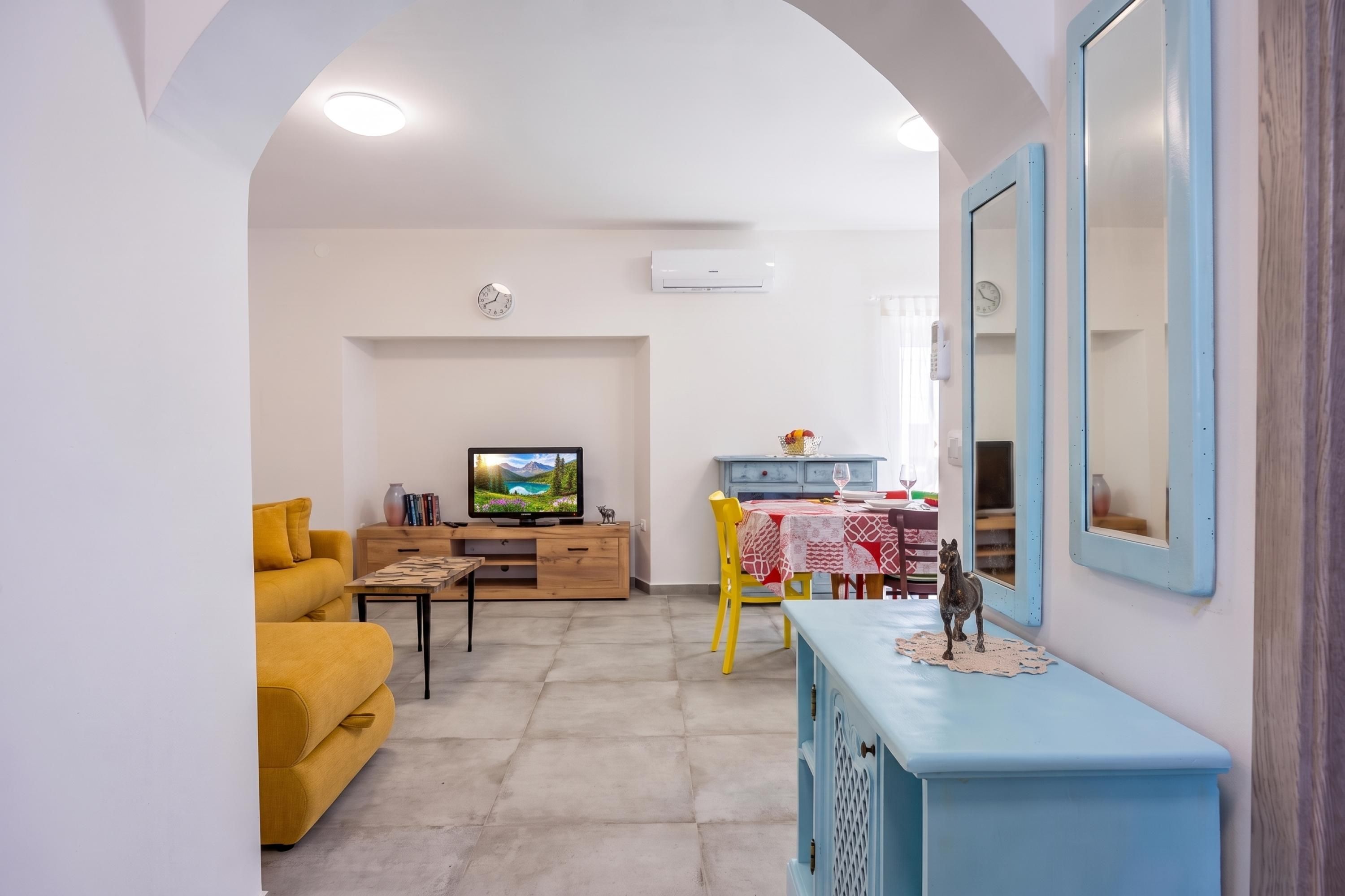 A living room with a sofa, a TV, a dining table with chairs, and a blue cabinet.