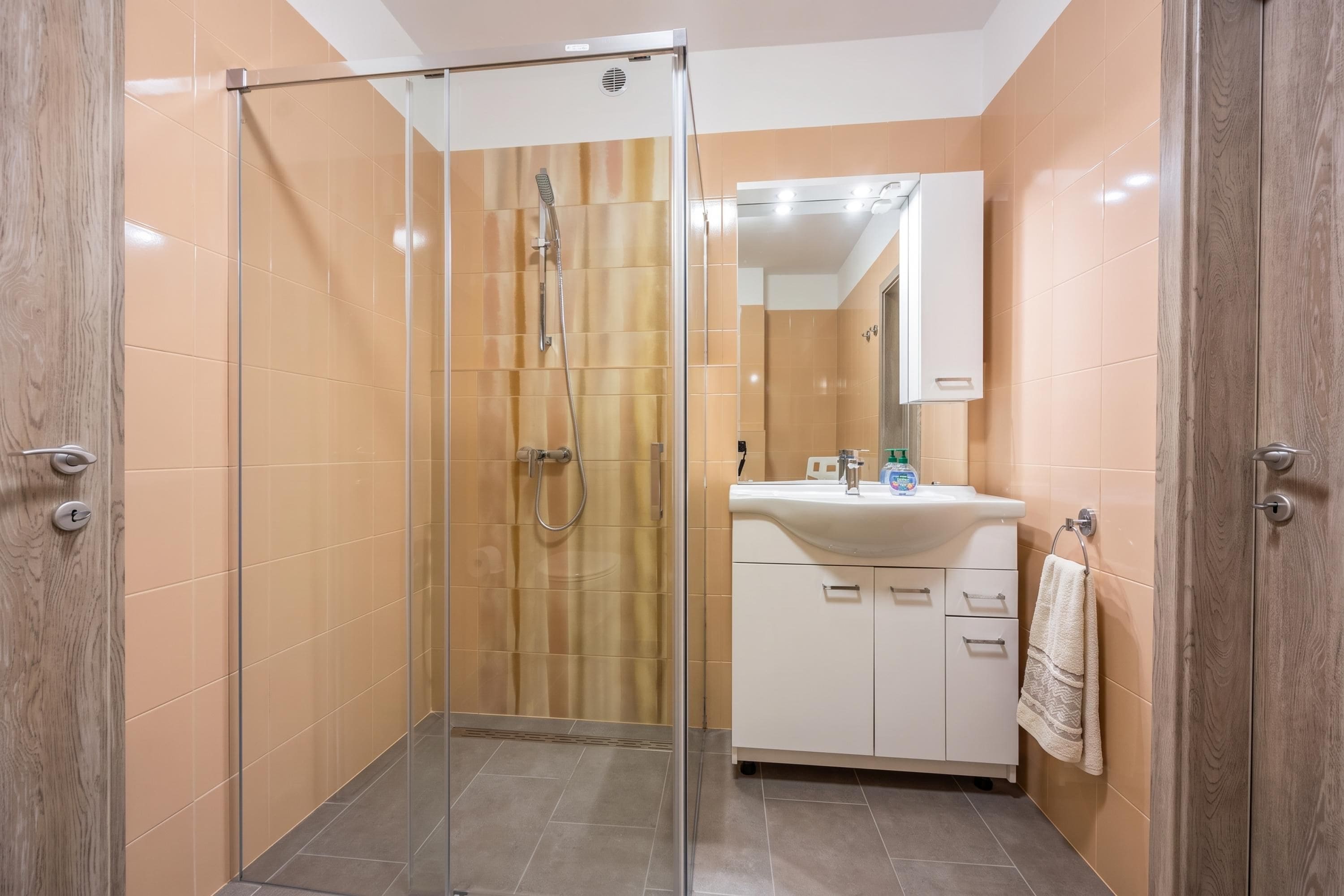 A modern bathroom with a glass-enclosed shower, a white sink with a mirror above it, and a towel hanging on the wall.