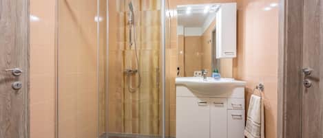 A modern bathroom with a glass-enclosed shower, a white sink with a mirror above it, and a towel hanging on the wall.