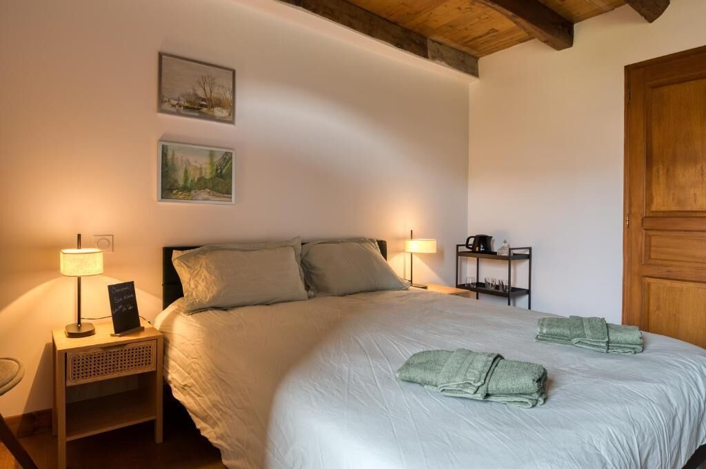 A bedroom with a bed, two bedside lamps, a nightstand, a shelf with toiletries, and a door.
