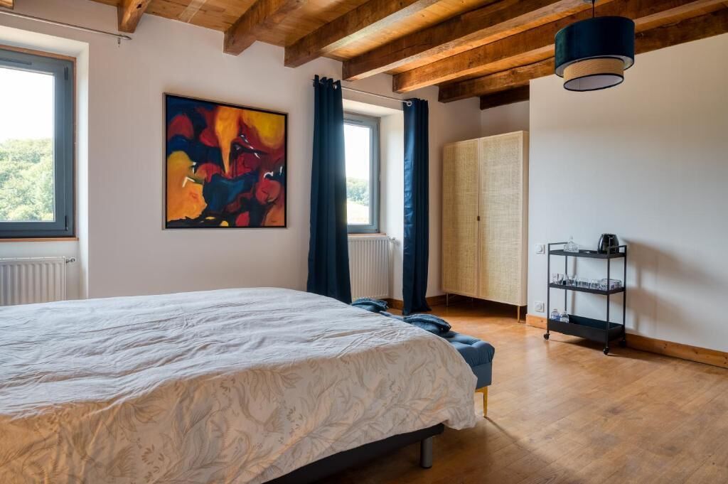 A bedroom with a large bed, a window, a radiator, a wooden ceiling, and a painting on the wall.