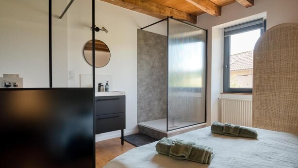 Ein modernes Schlafzimmer mit Bett, begehbarer Dusche, rundem Spiegel und Fenster.